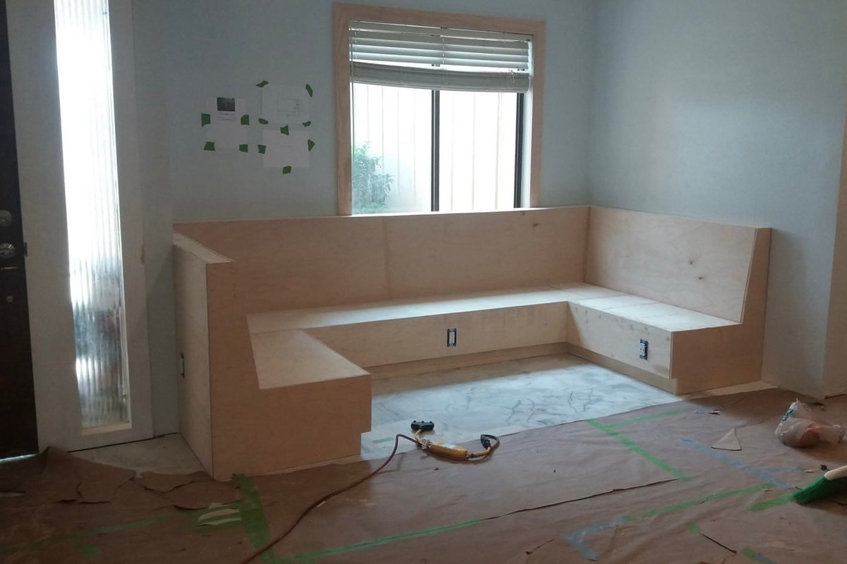 L-shaped built-in bench seat of plywood panels under a window in a light blue living room
