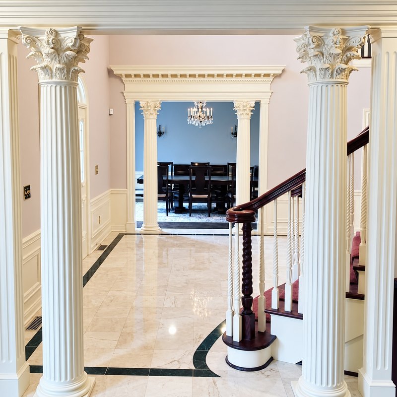 Front hall with two cream fluted columns, a dentil header, and a curved stair railing in the next room
